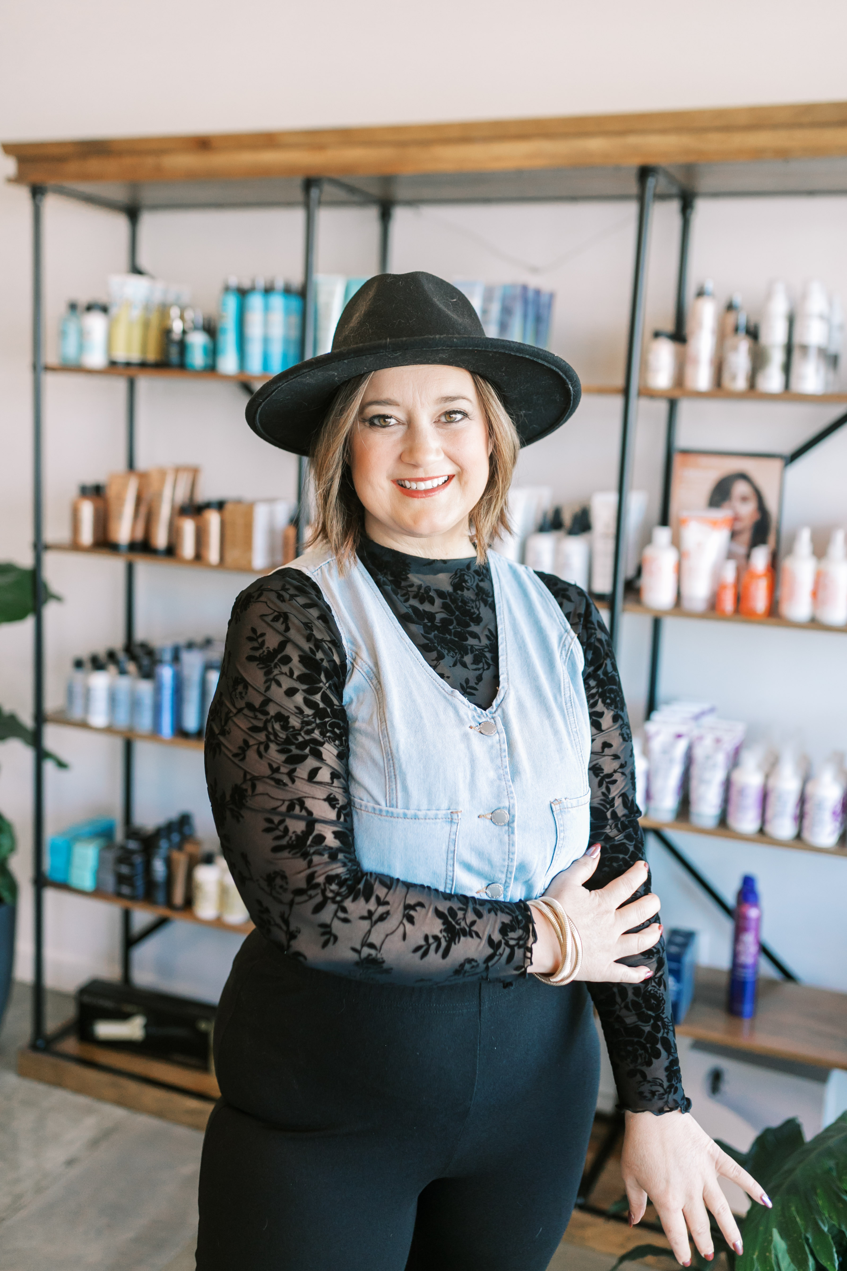 Stylist in black hat and white vest posing in fron of products