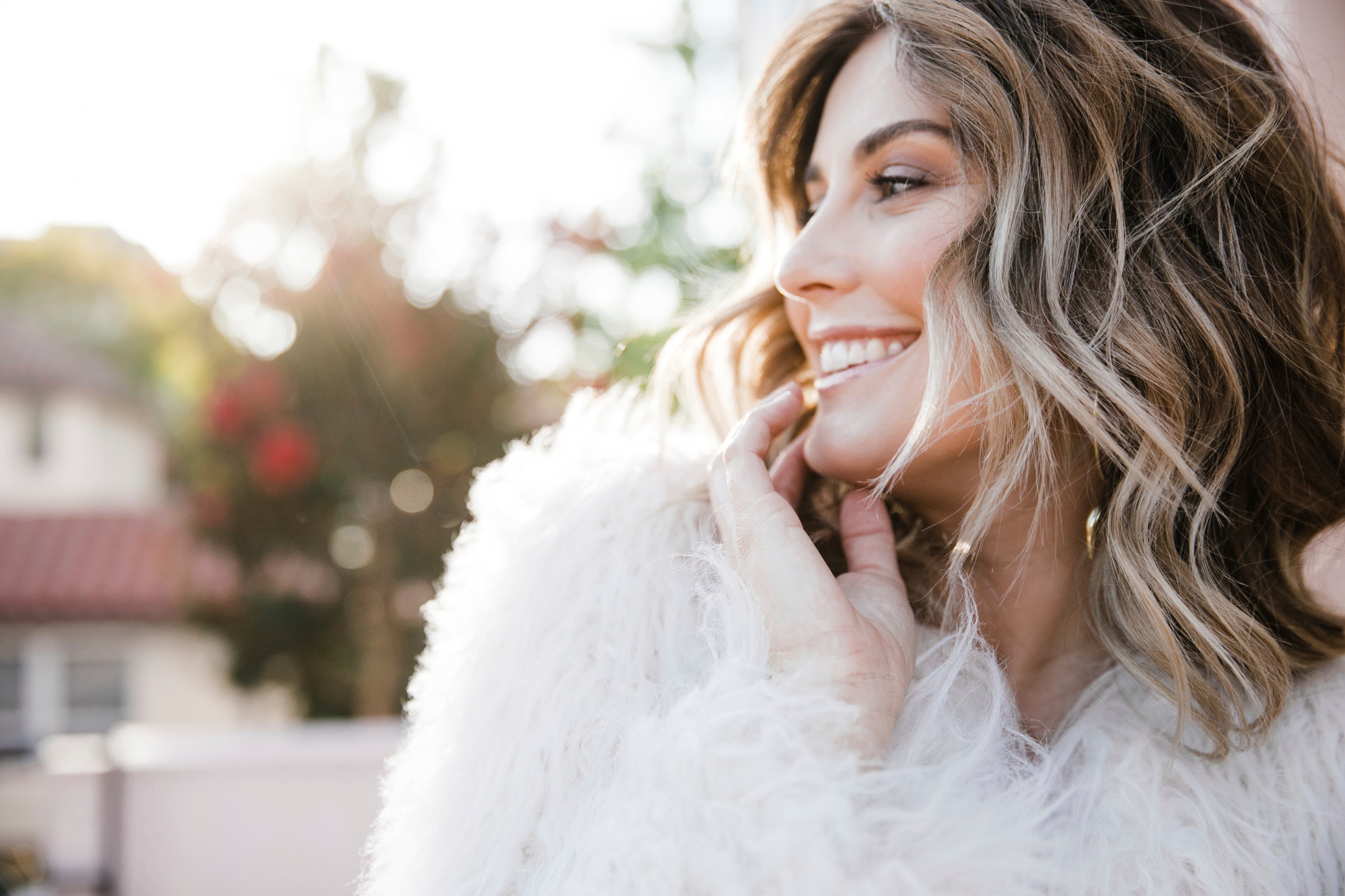Woman with long, wavy balayage hair smiling in a white faux-fur coat