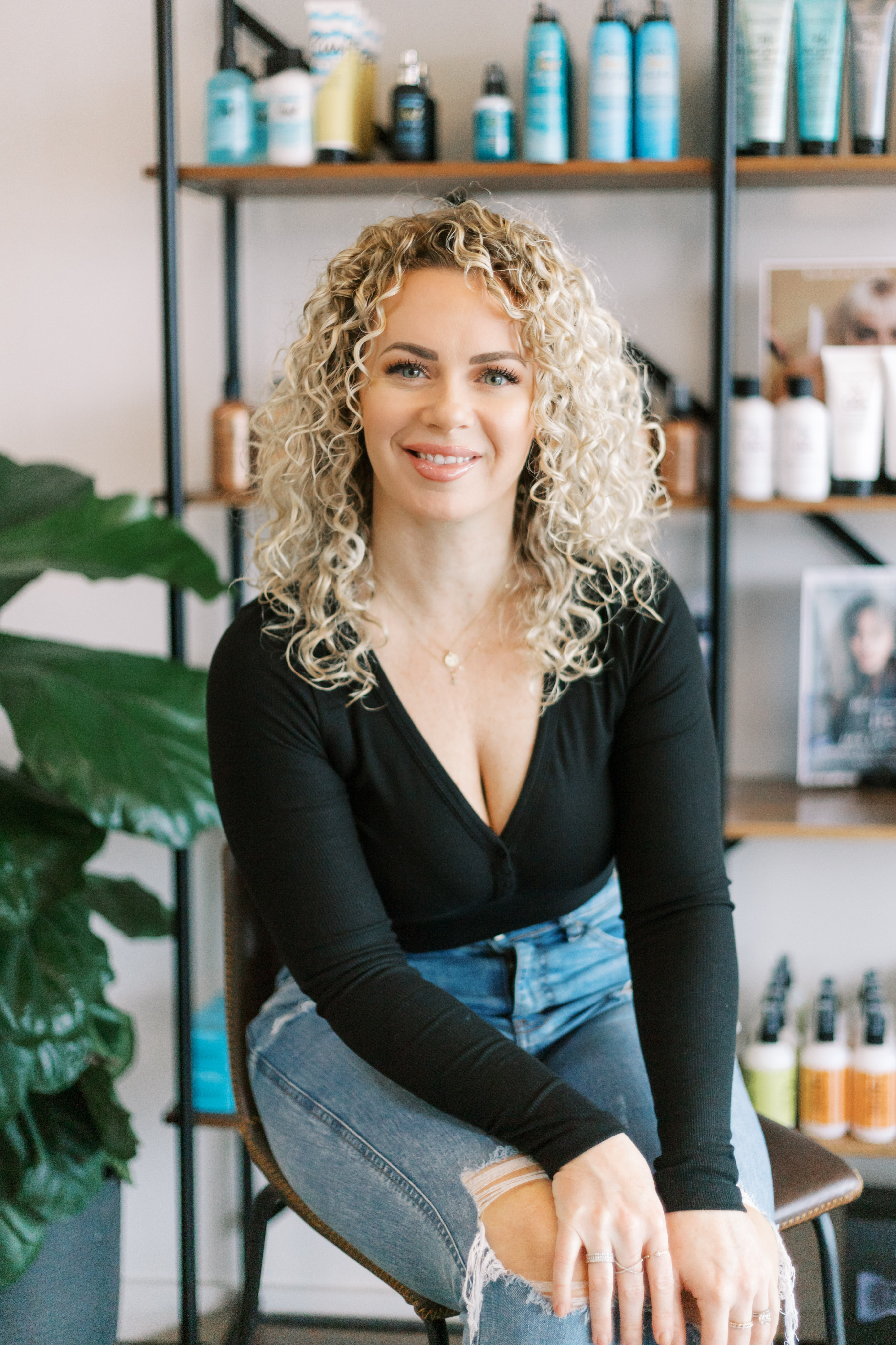 Stylist in black blouse and jeans seated in fron of products